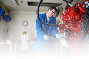 Researcher in a blue lab coat working with engine testing equipment at CE-CERT.