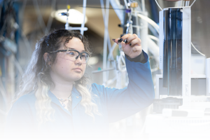 Student in a blue lab coat examining a scientific sample inside a research laboratory at UC Riverside.