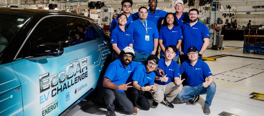 The UCR EcoCAR team gathers for a group photo next to their Cadillac LYRIQ in the workshop, all wearing matching blue team polos and smiling for the camera.