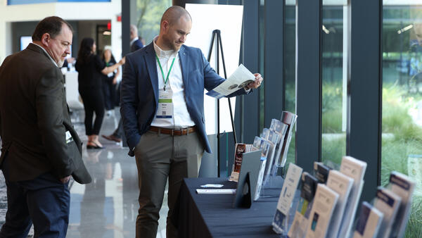 Conference attendee reads a brochure at the sponsor materials table during the Inaugural Hydrogen Engine Alliance – North America Conference, with additional attendees visible in the background.