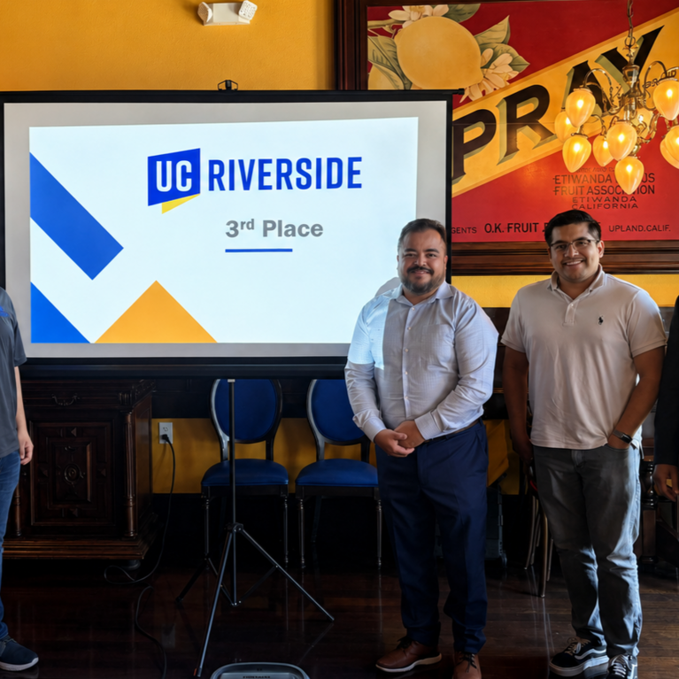 Four individuals stand beside a presentation screen displaying the UC Riverside logo and “3rd Place” during an awards recognition event held in a restaurant banquet room.