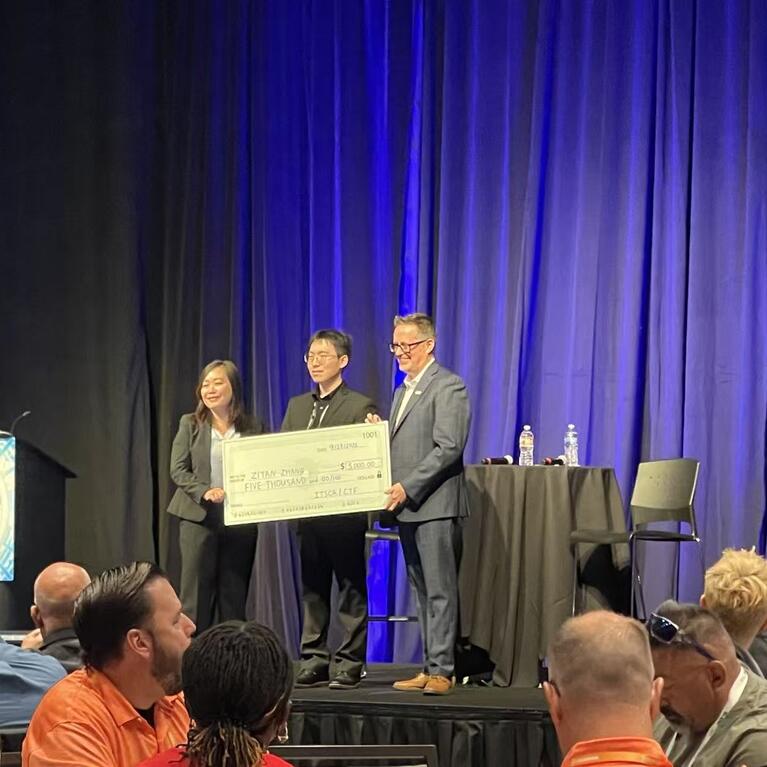 Ziyan Zhang holds a $5,000 scholarship check with two presenters onstage at the 2026 ITS California conference.