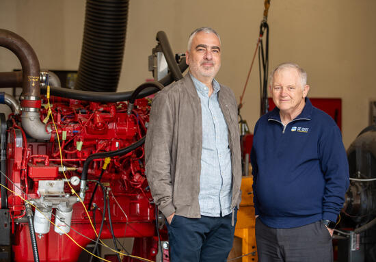  "Georgios Karavalakis and Wayne Miller stand in front of a large red hydrogen internal combustion engine, posing together during the announcement of the Hydrogen Engine Alliance of North America (H2EA-NA).