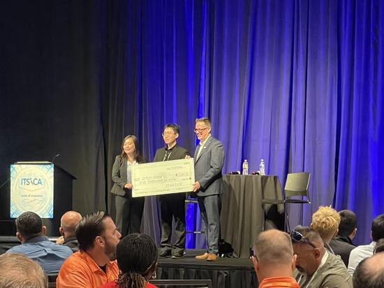 Ziyan Zhang holds a $5,000 scholarship check with two presenters onstage at the 2026 ITS California conference.