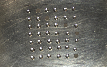 Close-up of three water droplets and a single dark spot on a textured metallic surface, part of aerosol group research on ATD INP.